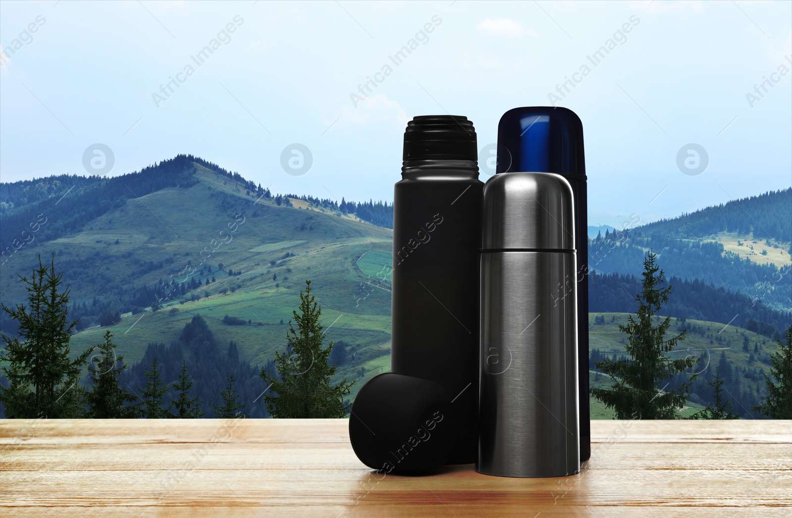 Image of Wooden desk with thermoses and mountain landscape on background