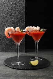 Photo of Tasty shrimp cocktail with sauce in glasses and lime on grey textured table