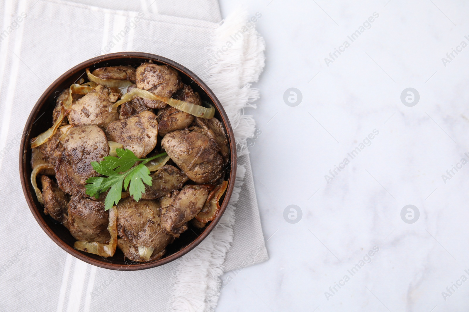 Photo of Tasty fried chicken liver with onion and parsley in bowl on white marble table, top view. Space for text