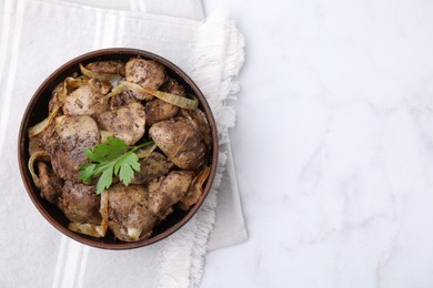 Tasty fried chicken liver with onion and parsley in bowl on white marble table, top view. Space for text