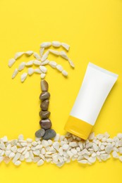 Photo of Suntan cream and palm made of marble pebbles on yellow background, flat lay