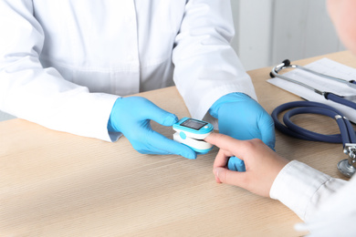 Photo of Doctor examining patient with modern fingertip pulse oximeter at wooden table, closeup