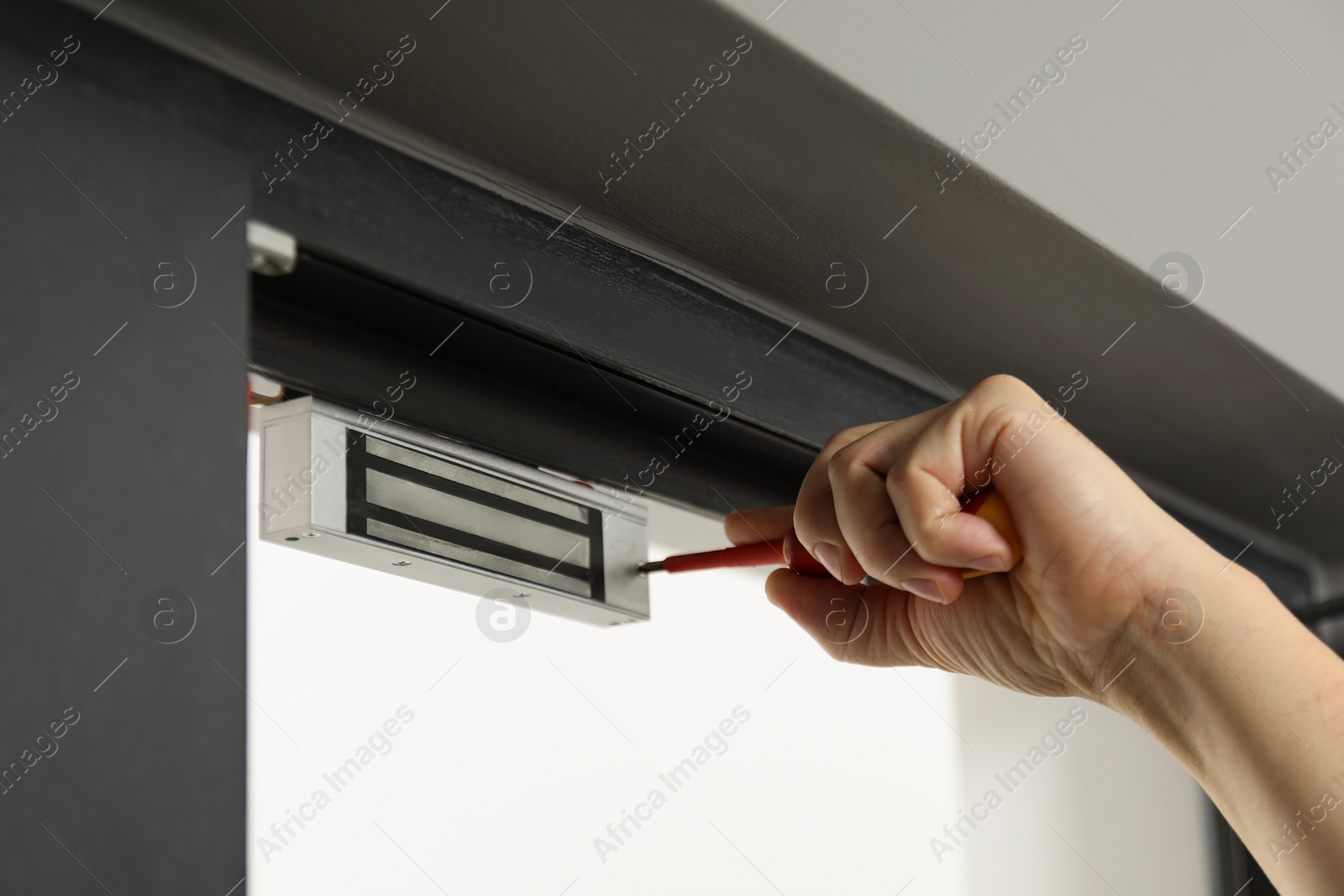 Photo of Man with screwdriver installing electromagnetic door lock indoors, closeup. Home security