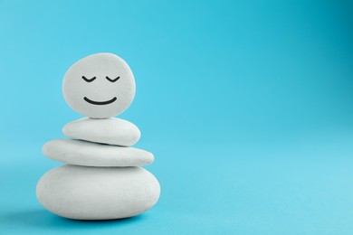 Photo of Stack of stones with drawn happy face on light blue background, space for text. Zen concept