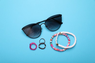 Stylish sunglasses, bracelets and rings on light blue background, flat lay