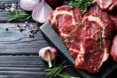 Photo of Fresh raw meat steaks on black wooden table, flat lay