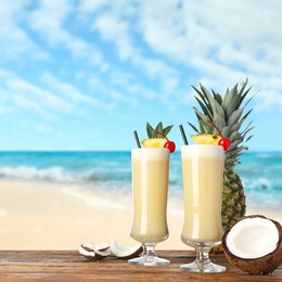 Image of Tasty Pina Colada cocktail on wooden table near ocean 