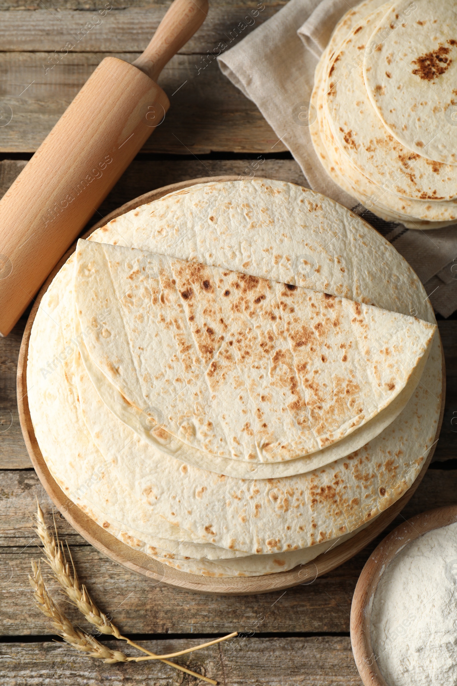 Photo of Tasty homemade tortillas, flour, rolling pin and spikes on wooden table, flat lay