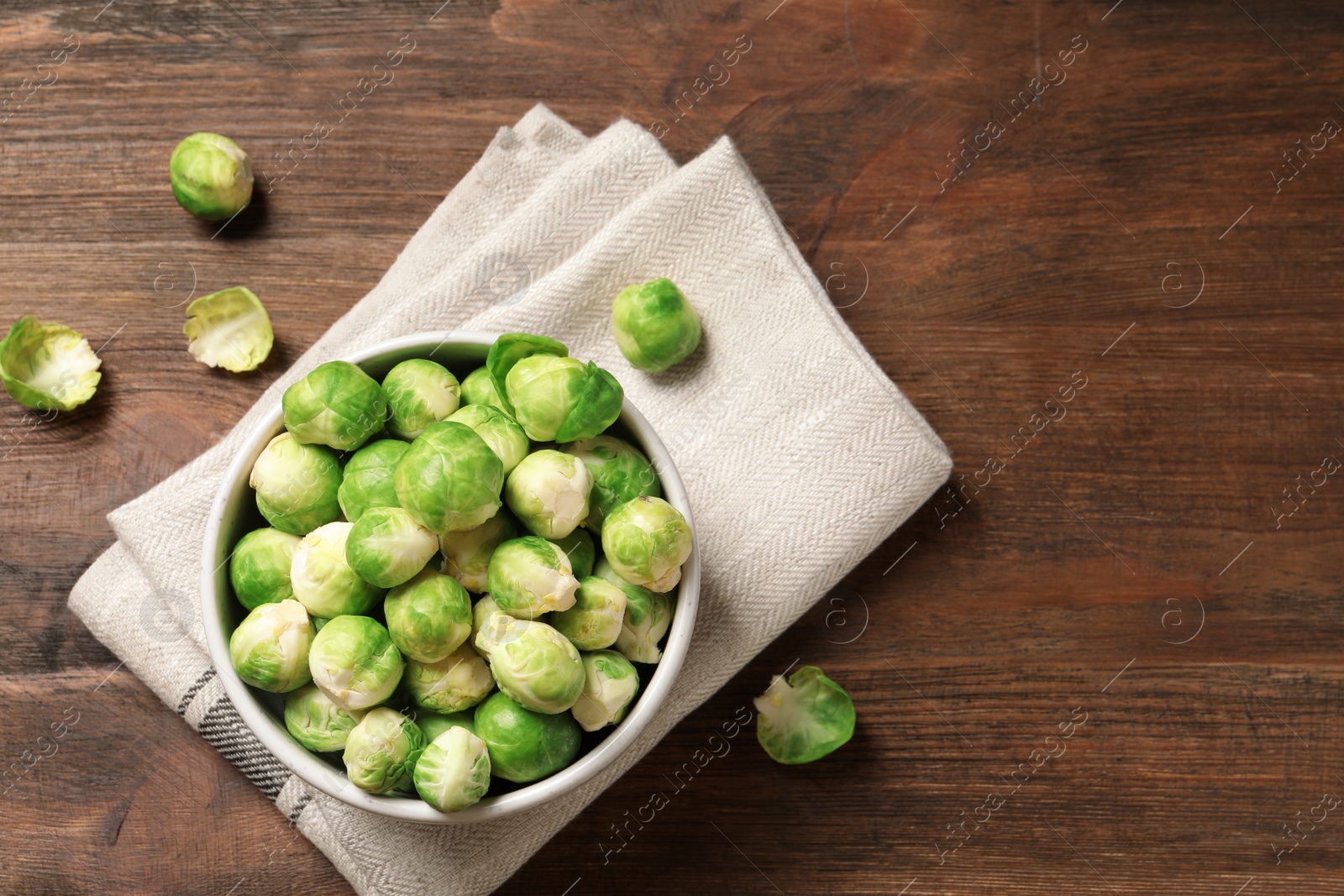 Photo of Bowl of fresh Brussels sprouts and napkin on wooden background, top view with space for text