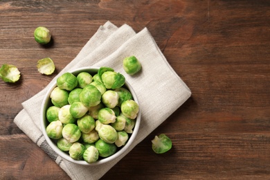 Bowl of fresh Brussels sprouts and napkin on wooden background, top view with space for text