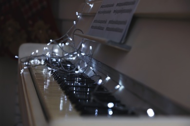 White grand piano with fairy lights and note sheets indoors, closeup. Christmas music