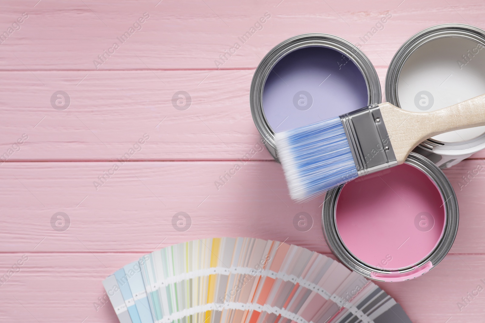 Photo of Cans of pastel paints, palette and brush on pink wooden table, flat lay. Space for text