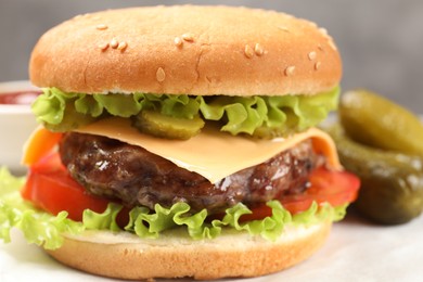 Photo of Tasty hamburger with patty and pickles on table, closeup