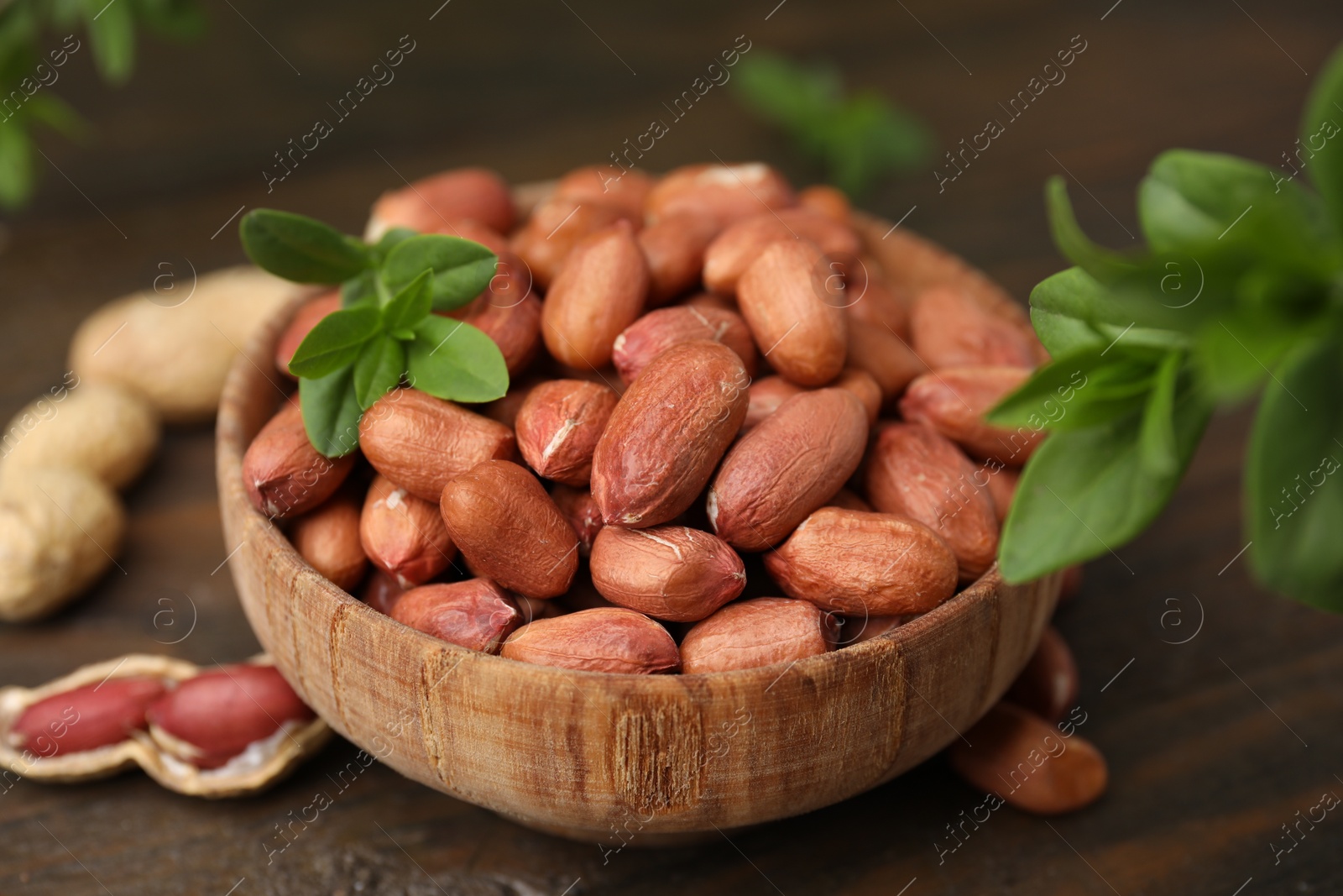 Photo of Fresh unpeeled peanuts and leaves in bowl on wooden table, closeup