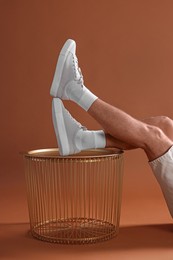 Photo of Man wearing stylish sneakers on table against brown background, closeup