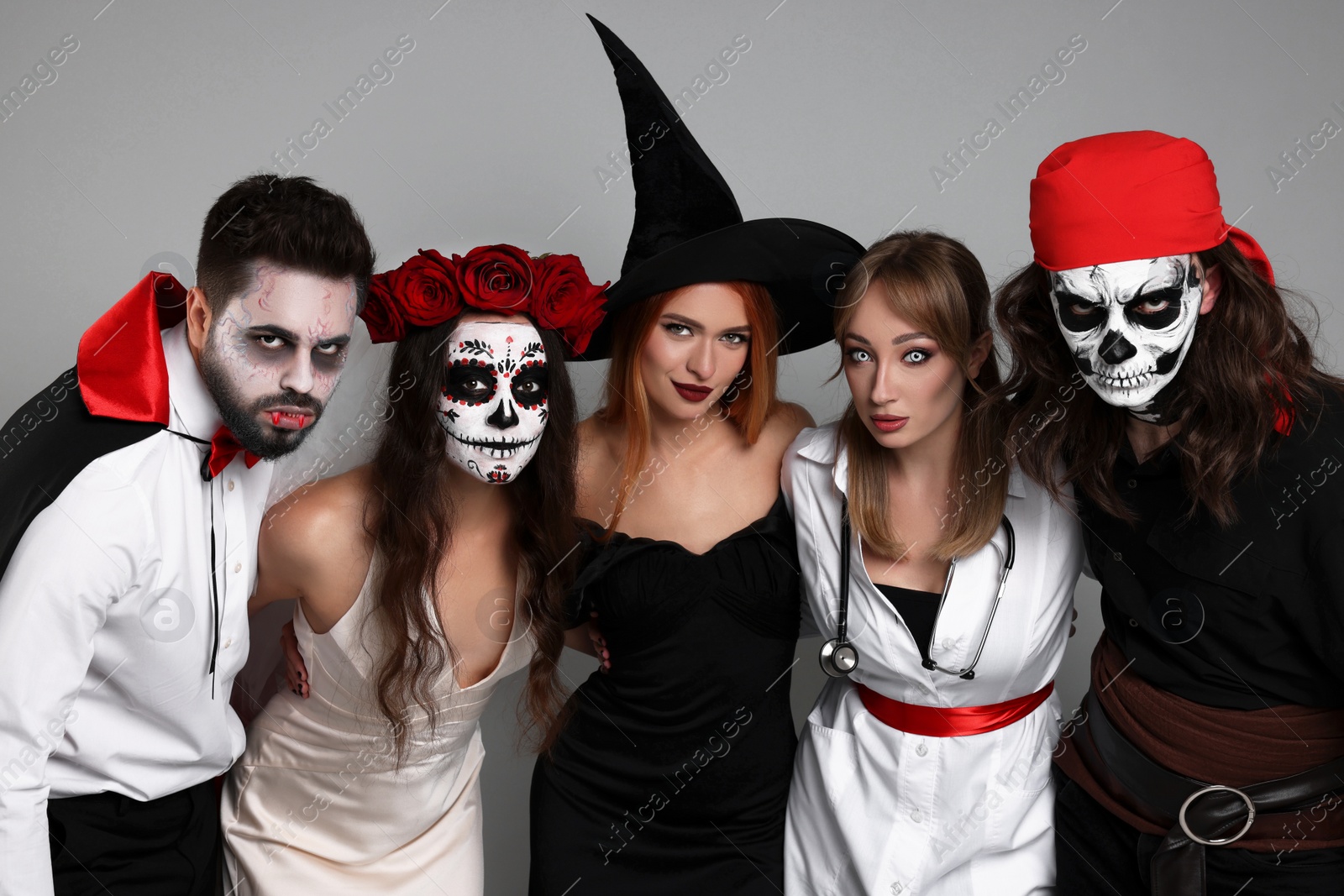Photo of Group of people in scary costumes on light grey background. Halloween celebration
