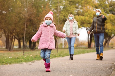 Family in medical masks walking outdoors on autumn day. Protective measures during coronavirus quarantine