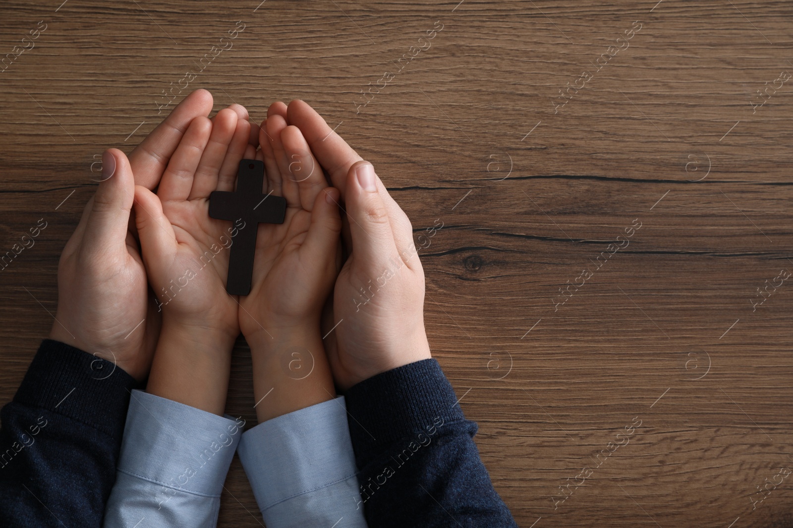 Photo of Boy and his godparent holding cross at wooden table, closeup