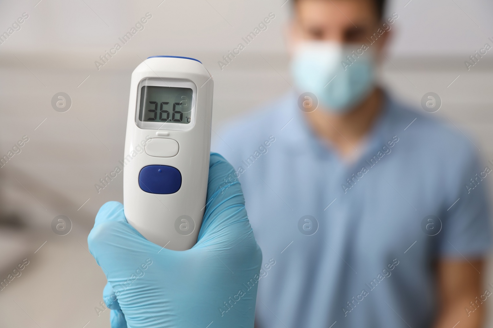 Photo of Doctor measuring man's temperature indoors, closeup. Prevent spreading of Covid-19