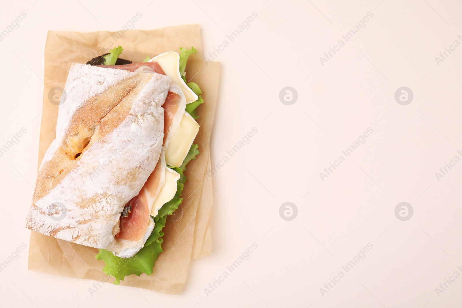 Photo of Tasty sandwich with brie cheese and prosciutto on beige background, top view. Space for text