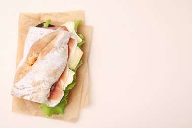 Photo of Tasty sandwich with brie cheese and prosciutto on beige background, top view. Space for text