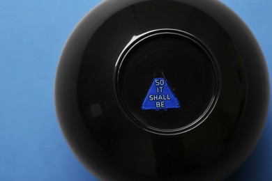Photo of Magic eight ball with prediction So It Shall Be on blue background, above view