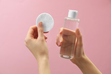 Woman holding makeup remover and cotton pad on pink background, closeup