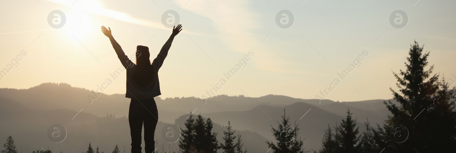 Image of Silhouette of woman at sunrise in mountains, back view. Banner design