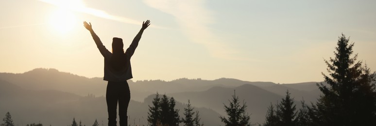 Image of Silhouette of woman at sunrise in mountains, back view. Banner design