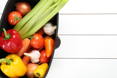 Photo of Black pot with fresh vegetables on white wooden table, top view. Space for text