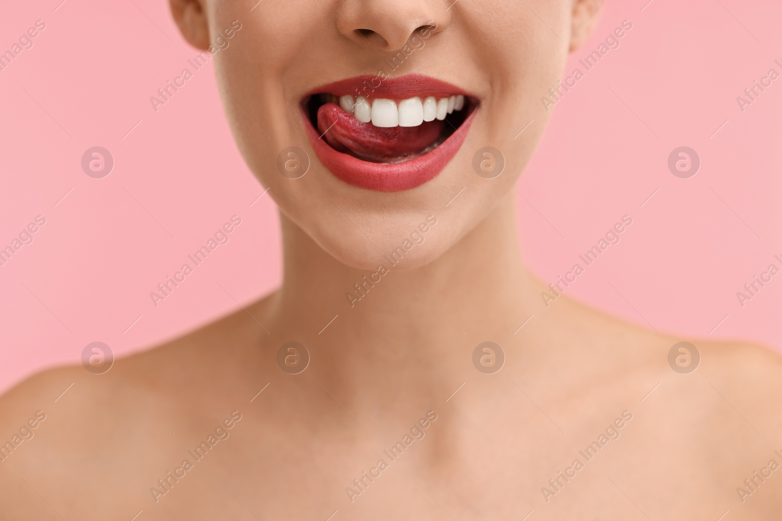 Photo of Woman with beautiful lips licking her teeth on pink background, closeup