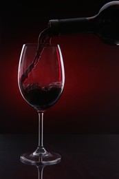 Photo of Pouring red wine from bottle into glass on color background