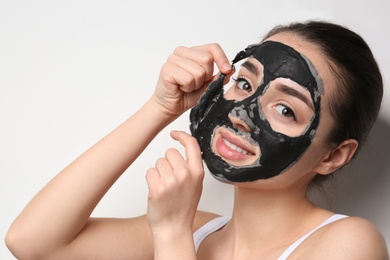 Photo of Beautiful young woman removing black mask from her face on white background