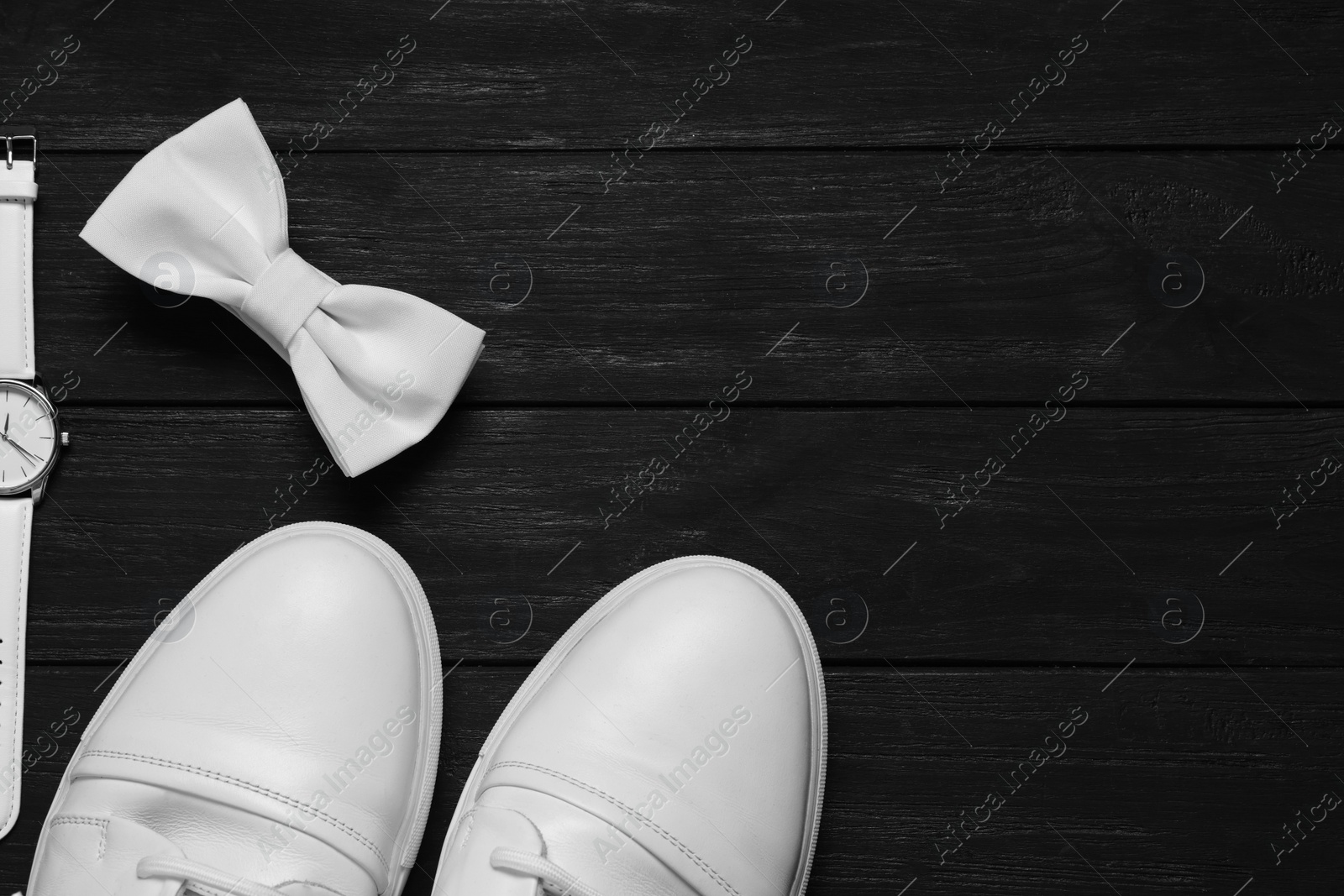 Photo of Stylish white bow tie, shoes and wristwatch on black wooden background, flat lay. Space for text