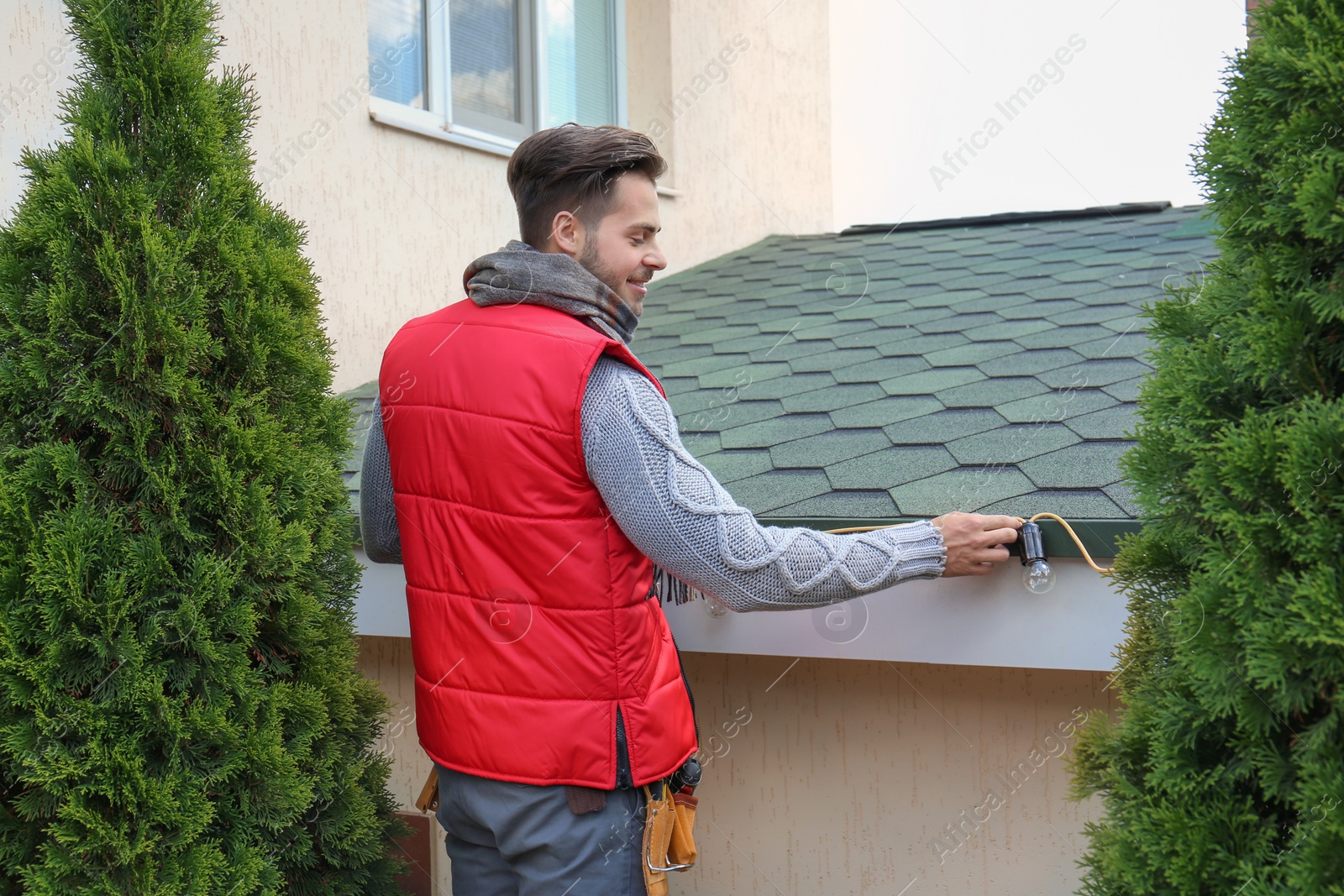 Photo of Young man decorating roof with Christmas lights