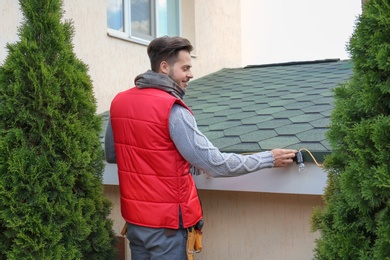 Young man decorating roof with Christmas lights