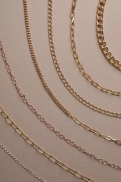 Different metal chains on light brown background, flat lay. Luxury jewelry