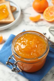 Photo of Tasty tangerine jam in glass jar on white marble table, space for text