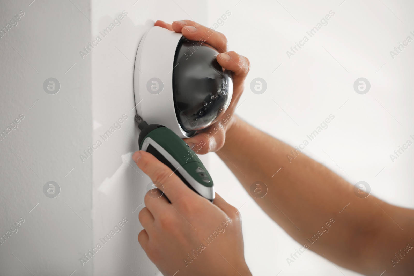 Photo of Technician installing CCTV camera on wall indoors, closeup