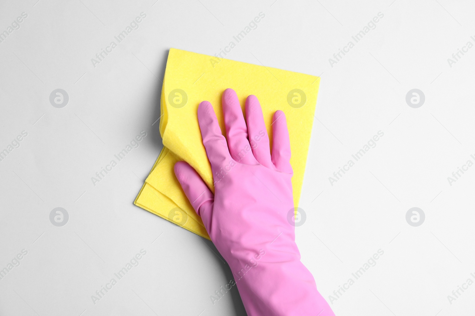 Photo of Person in rubber glove with rag on light grey background, closeup of hand