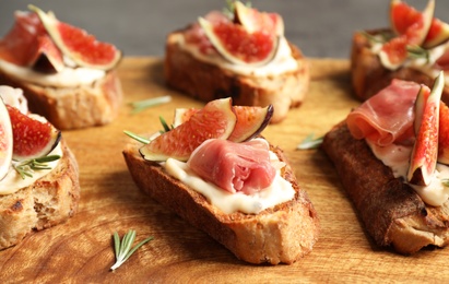 Photo of Bruschettas with cream cheese, prosciutto and figs served on wooden board, closeup