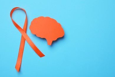 Photo of Orange ribbon and paper brain cutout on light blue background, flat lay with space for text. Multiple sclerosis awareness