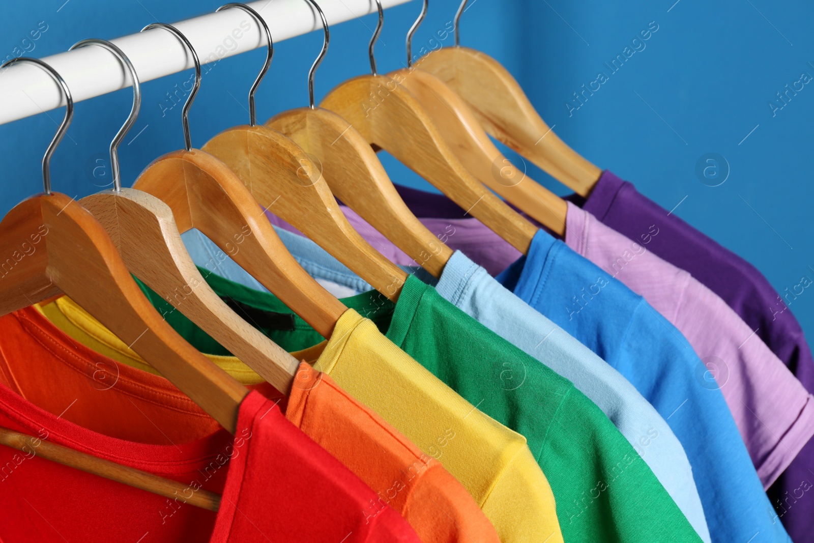 Photo of Bright clothes on hangers against blue background, closeup. Rainbow colors