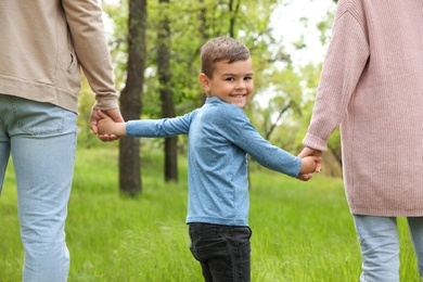 Happy little child holding hands with his parents in park. Family weekend