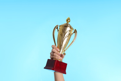 Photo of Woman holding gold trophy cup on light blue background, closeup