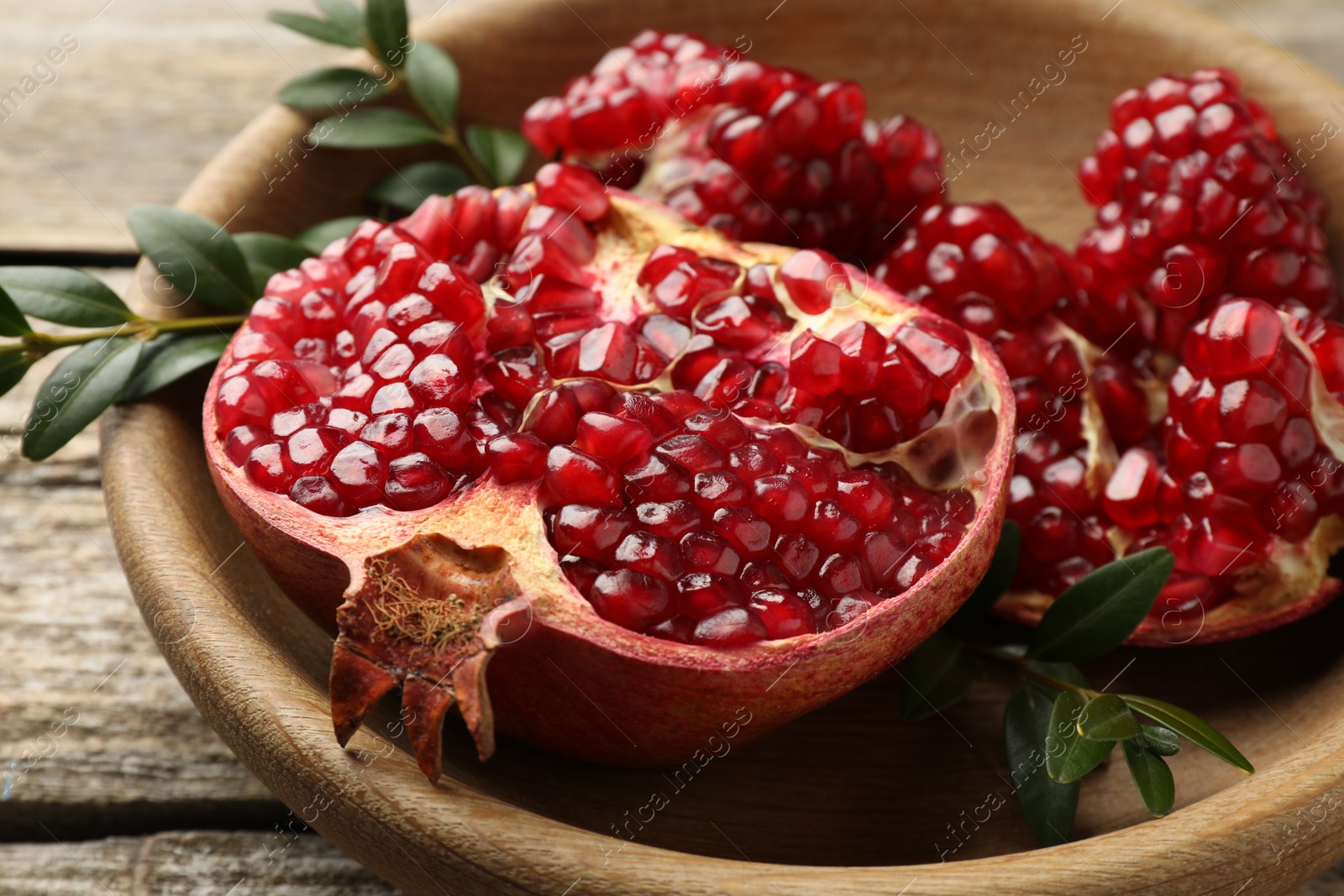 Photo of Cut fresh pomegranate and green leaves on wooden table, closeup