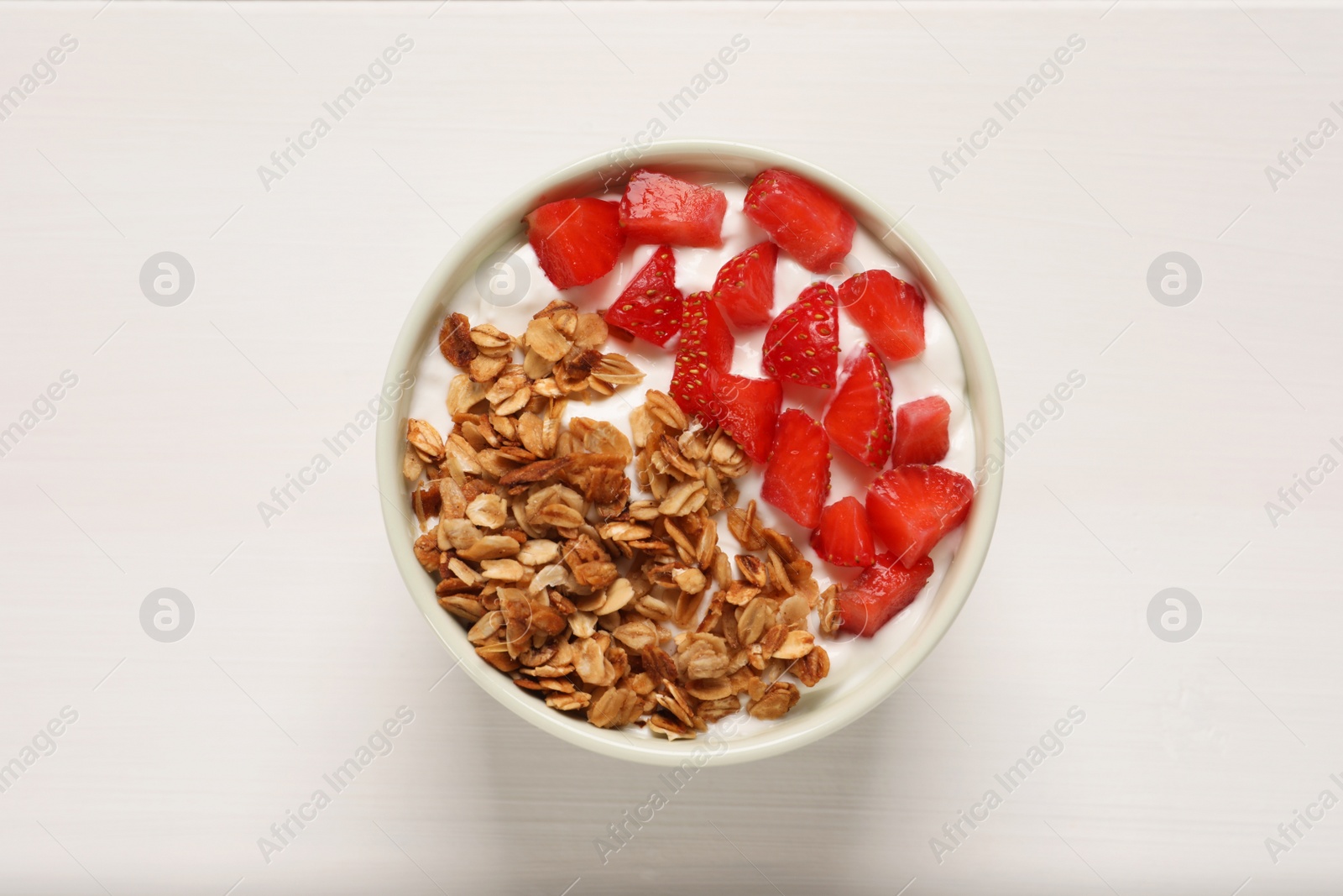 Photo of Yogurt served with granola and strawberries on white wooden table, top view