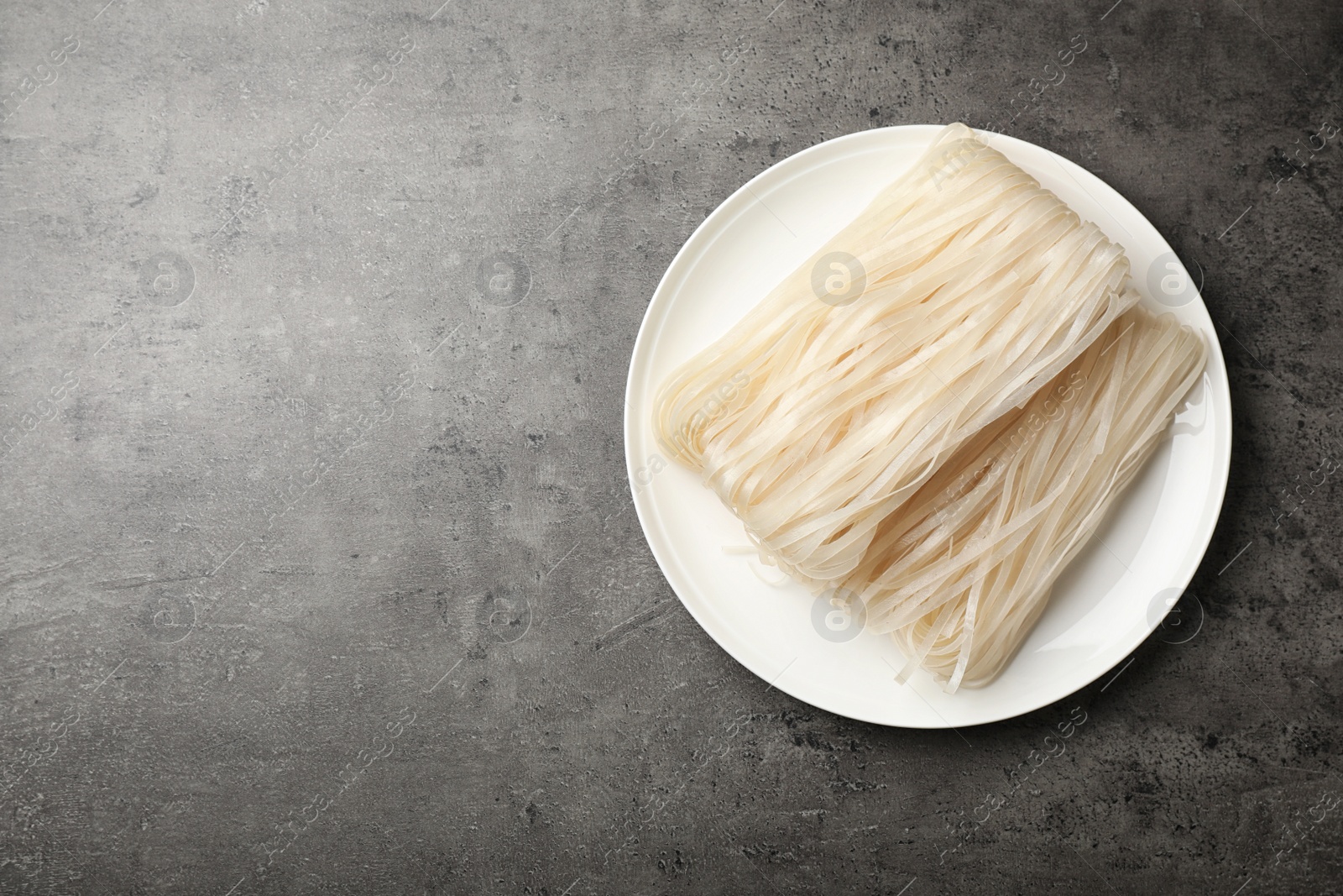 Photo of Plate with raw rice noodles on grey background, top view. Space for text