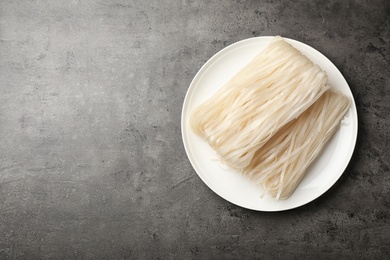 Plate with raw rice noodles on grey background, top view. Space for text