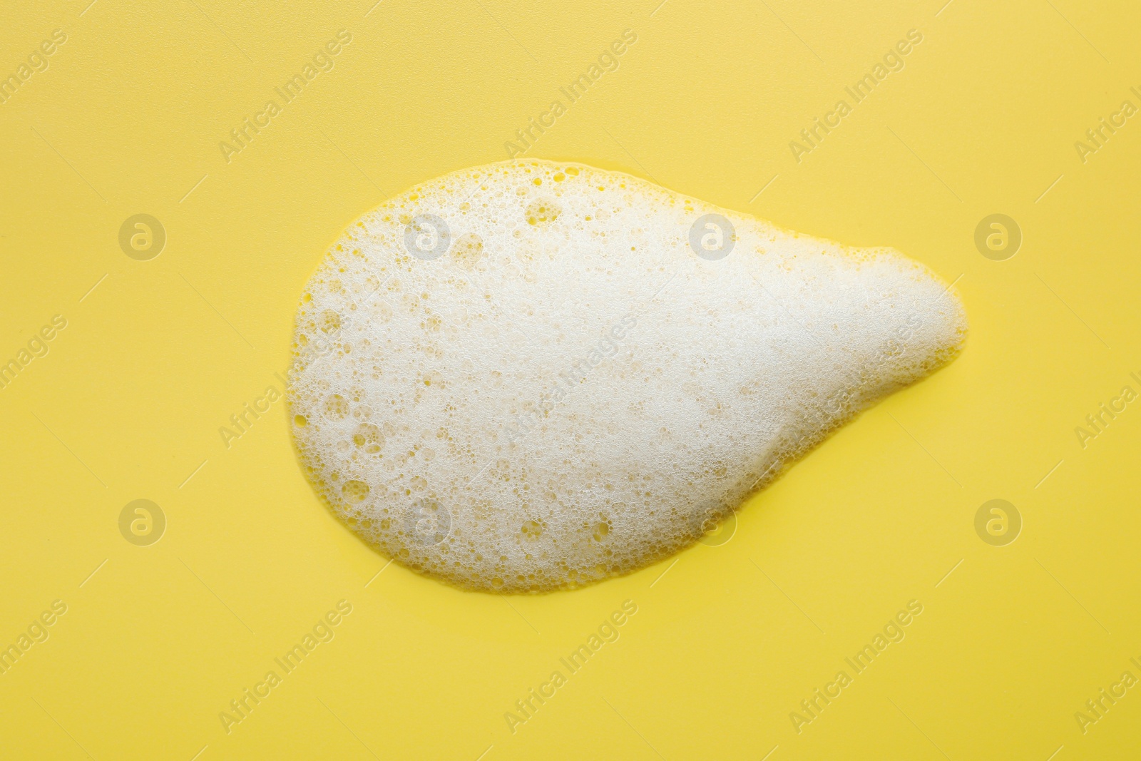 Photo of Drop of fluffy soap foam on yellow background, top view